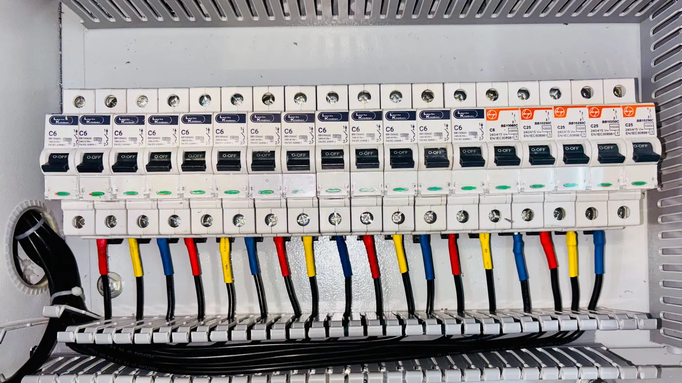 An electrical circuit breaker panel with rows of labelled breakers and colour-coded wiring